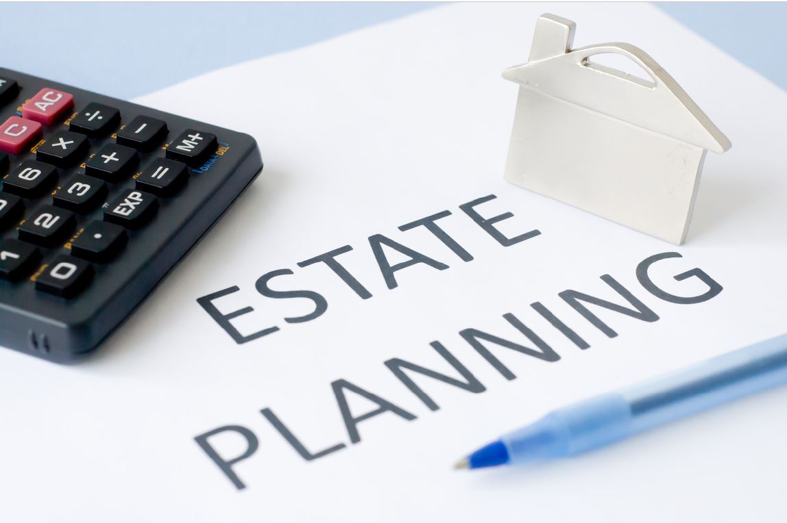 estate planning text on page with calculator, tiny model of house, and blue pen