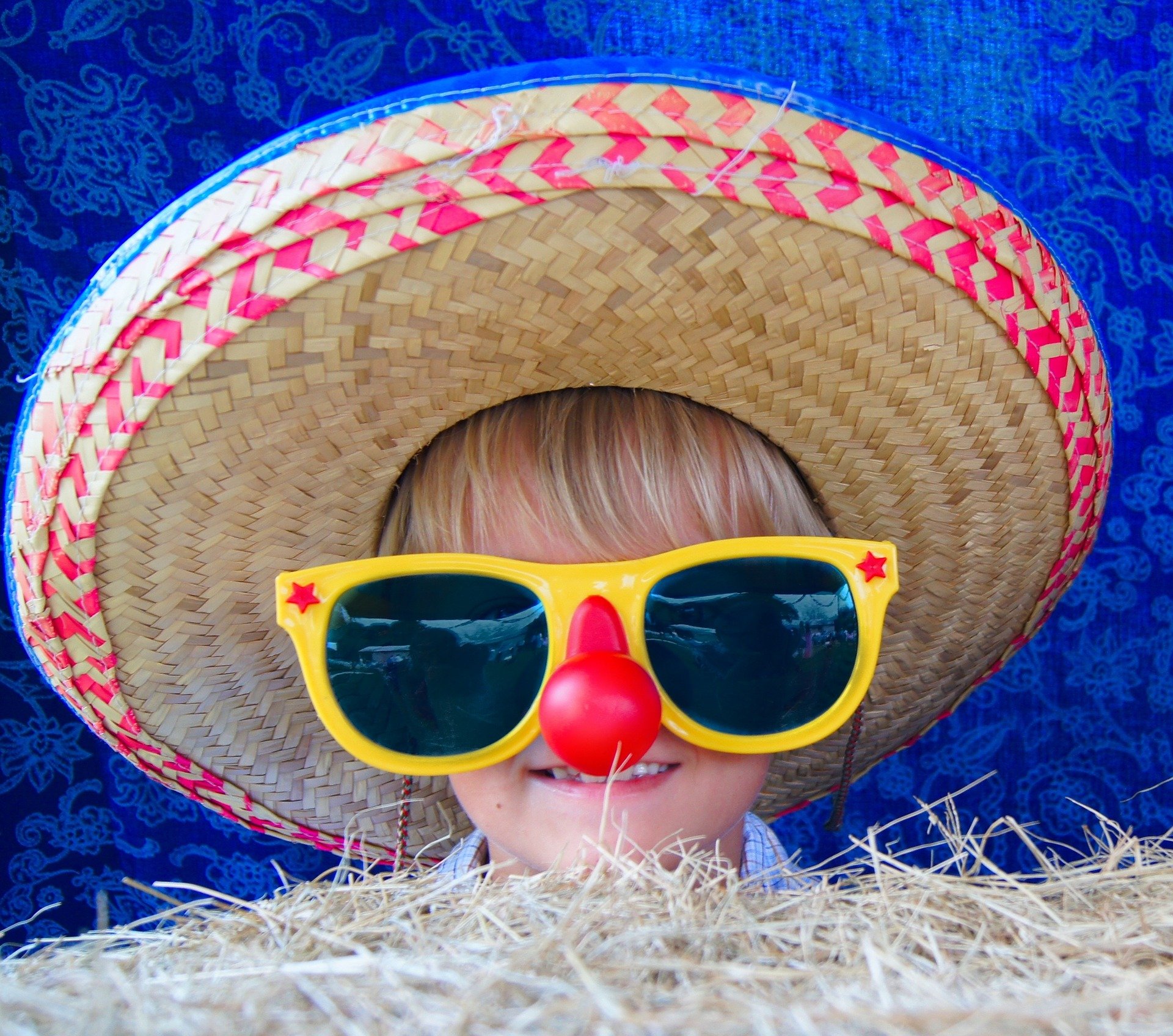 Child wearing a giant straw hat, clown nose and large oversized sunglasses