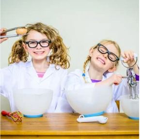 two children with bowls, whisks and safety goggles doing kitchen science