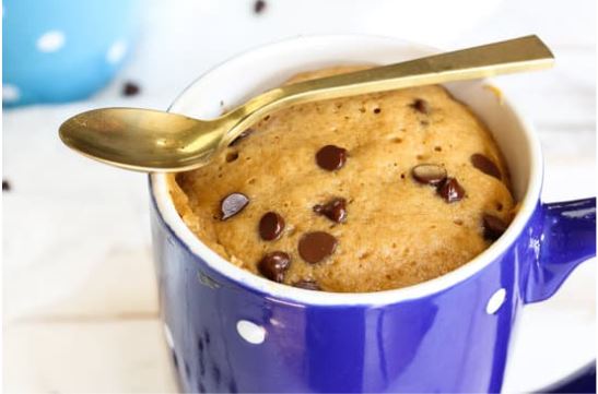 chocolate chip cake in a mug with a spoon resting across the top of the mug.