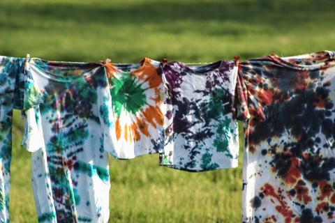 shirts with colored dye hanging on a line over grass