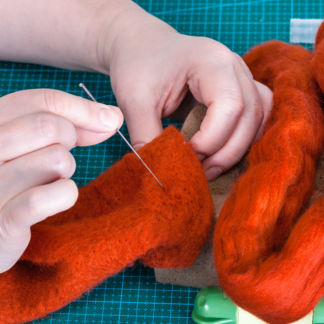 closeup of hands holding a needle poking orange felt