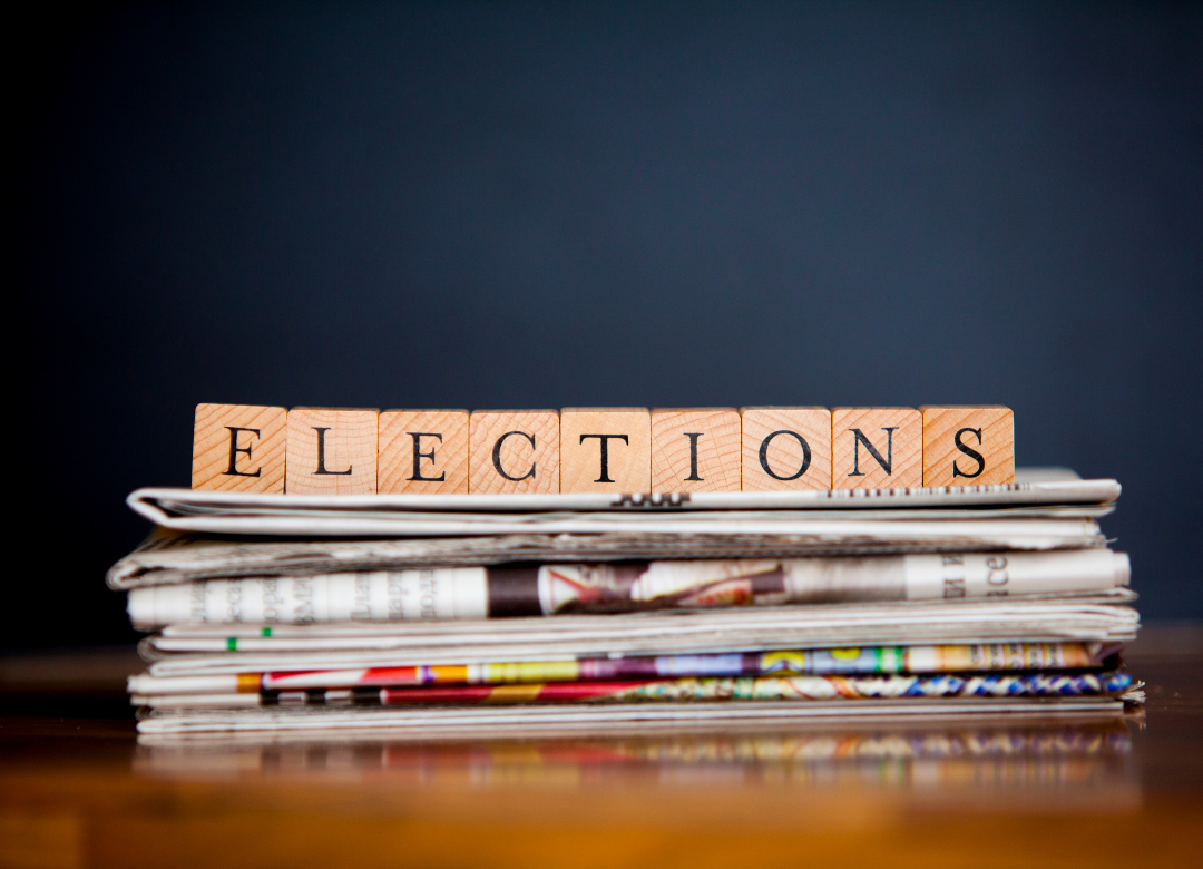 letter tiles spelling elections above a stack of newspapers