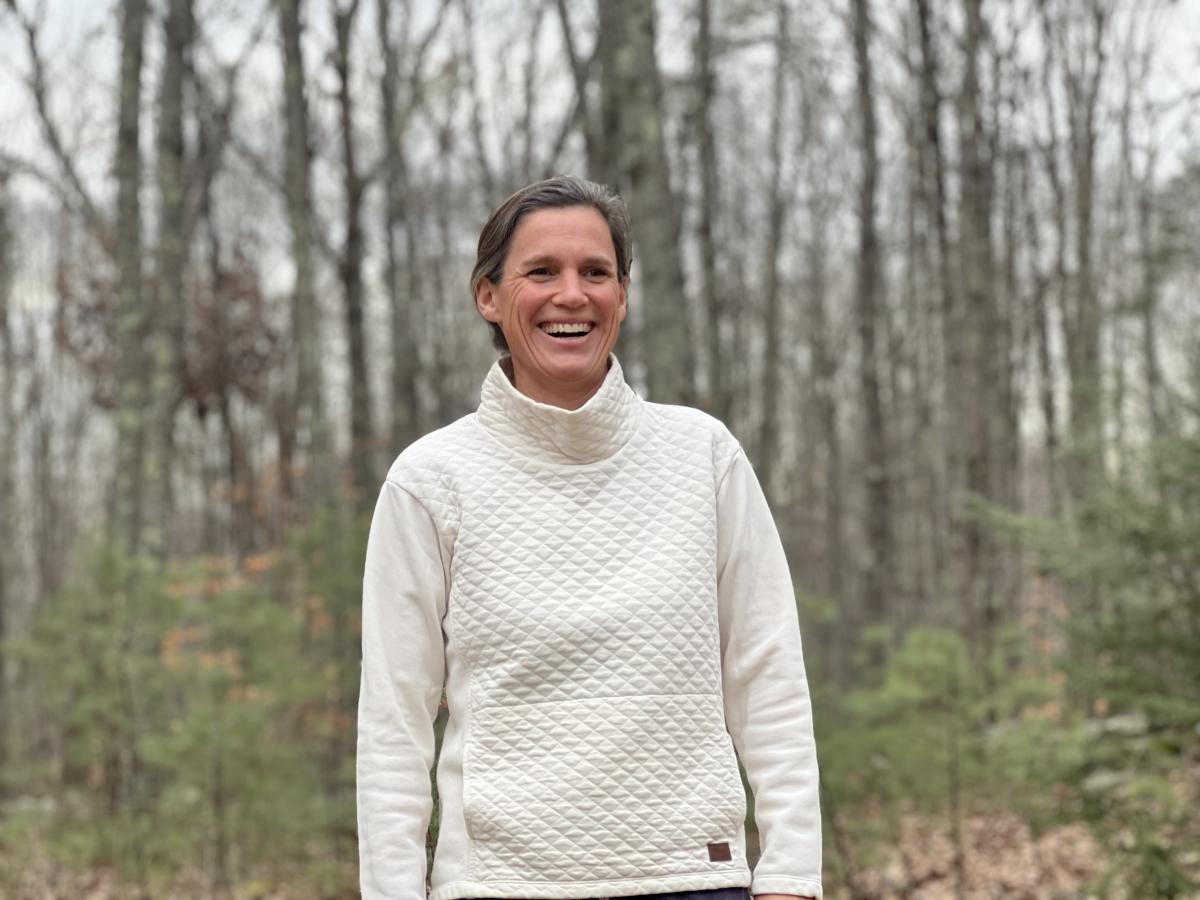 Photo of person in white sweater in front of trees in winter