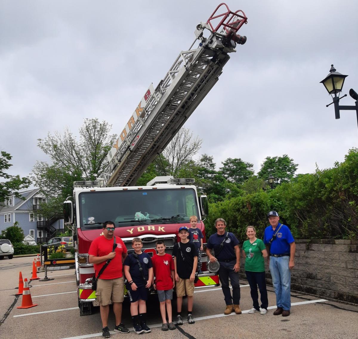 fire truck with people standing in front of it next to fire fighters.