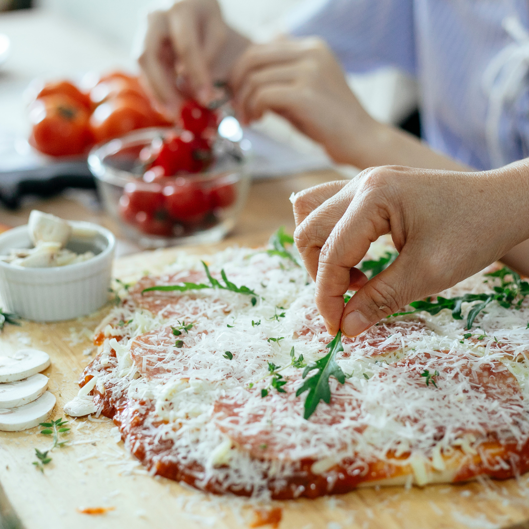 person adding fresh herbs to a homemade pizza